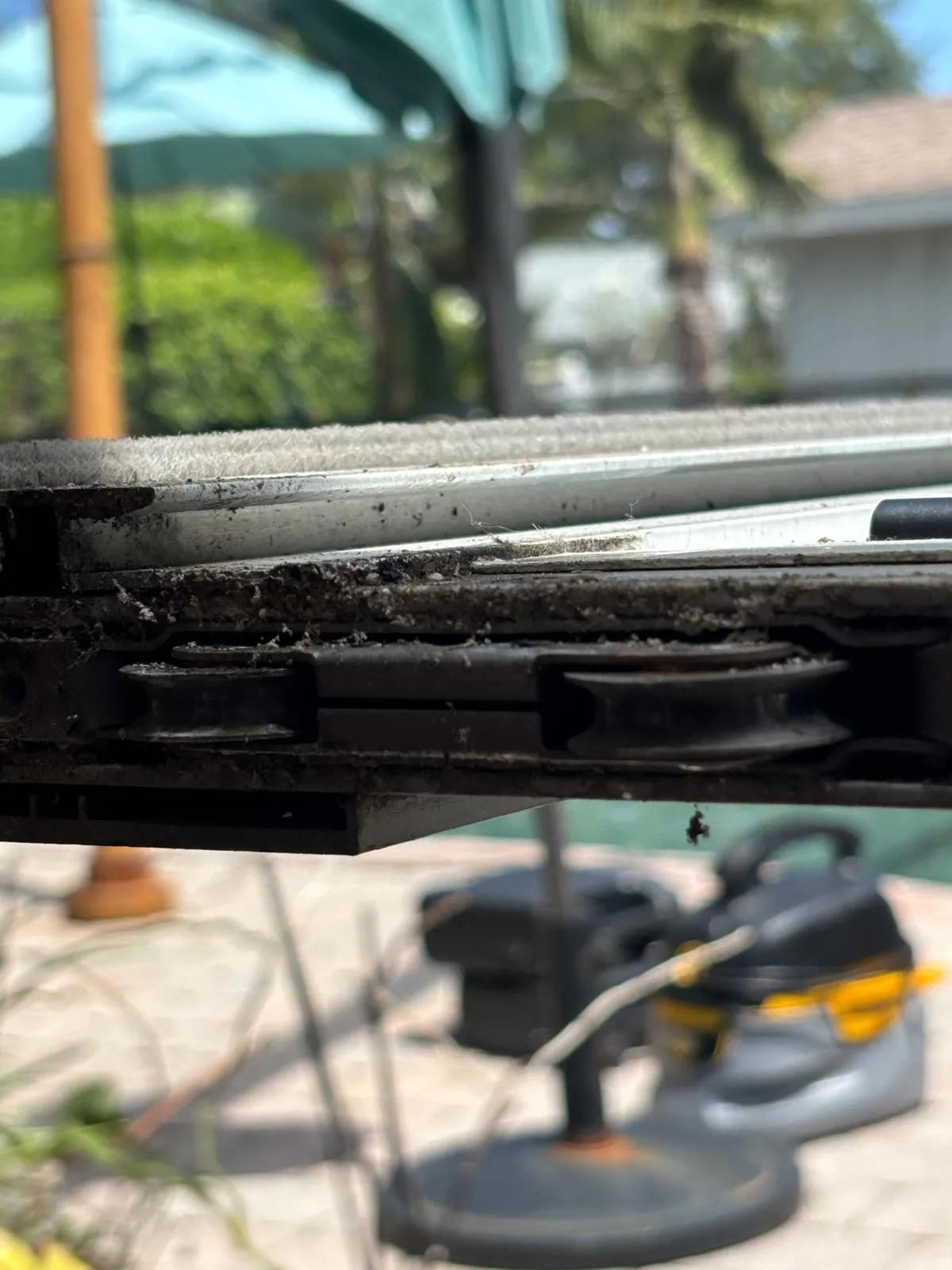 Close-up of worn sliding glass door rollers showing flat spots and debris buildup from years of use in South Florida